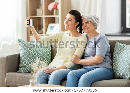 family, generation and people concept - happy smiling senior mother with adult daughter taking selfie by smartphone at home