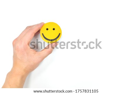 Happiness and positivity concept. Hand holding yellow smiling face in white background with copy space.