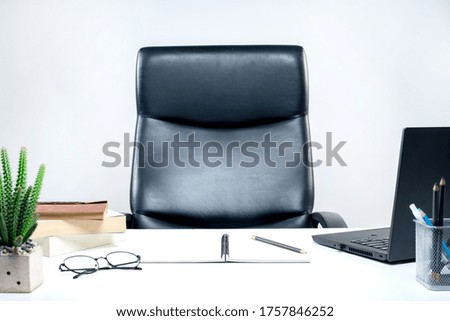 Picture of a desk with a laptop computer and workbook and a stack of books Resting on a desk in a white office.