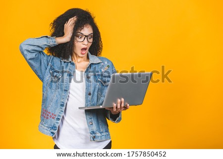 Shocked amazed african american black business or student woman, posing isolated on yellow background. Mock up copy space. Working on laptop pc computer.