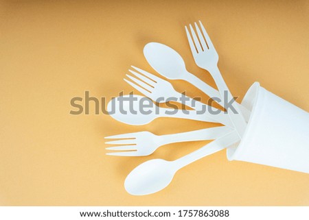 Plastic spoon and fork in a cup over orange background. Disposable utensil.