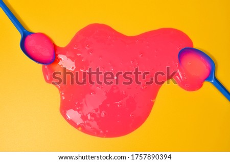 Shot of a classic blue colored spoon with pink sticky slime on yellow background. Minimalism in photography, concept creative picture. Painting tool