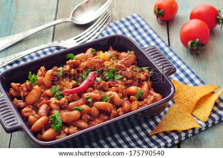 Chili Con Carne in baking mold with tortilla chips on wooden background