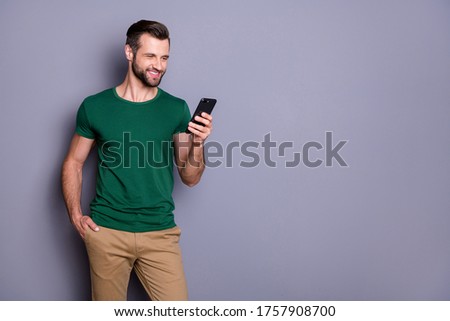 Portrait of positive cheerful guy addicted blogger use cellphone read social network information subscribe comment wear stylish outfit isolated over gray color background