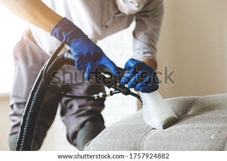 Man dry cleaner's employee hand in protective rubber glove cleaning sofa with professionally extraction method. Early spring regular cleanup. Commercial cleaning company concept. Closeup Royalty-Free Stock Photo #1757924882