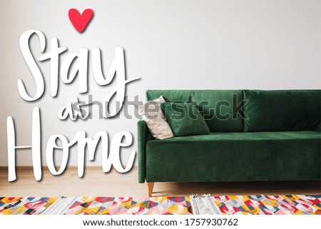 modern green sofa and pillows in living room with colorful rug near stay at home lettering