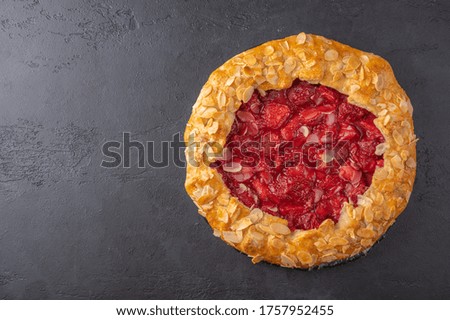 Homemade summer flan pie with strawberries and almond petals on dark background. Top view with copy space