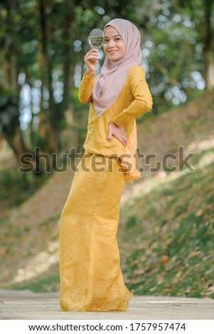 Portrait of a beautiful young muslim woman wearing hijab using  mirror with blurred background taken in outdoor. Using for Fashion and beauty concept