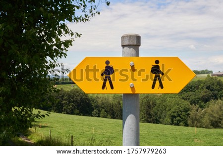 Bright yellow hiking trail signs arrows with two hiker figures pointing in opposite directions on an iron sign post in Switzerland.