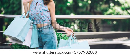 Shopper asian woman holding shopping bags. Her face with happy smile and wear blue shirt. Customer enjoy summer sale city lifestyle concept. Banner size background.
