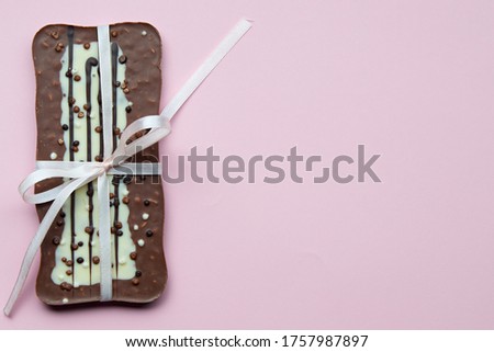 Close up of a milk chocolate bar with a rose ribbon or bow on pink background. 