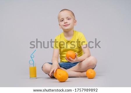 Smiling boy sitting with fruit orange and drink. Isolated on gray