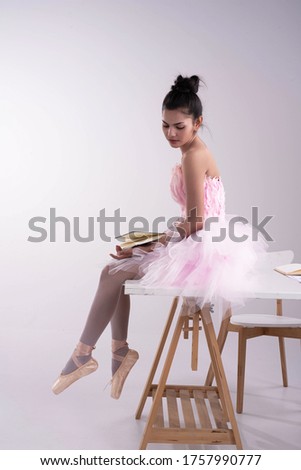 Young beautiful lady wearing pink ballet suit,sitting on wooden desk,model posing on background