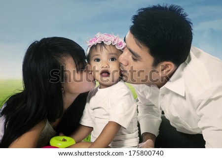 Happy mother and father kissing their daughter in the park