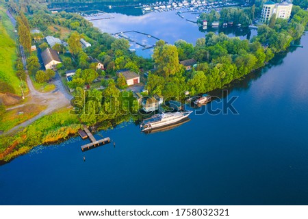 White Boat near the shore with a small river pier. River Boat near the Yacht Club on the dock. Aerial Drone Shot.