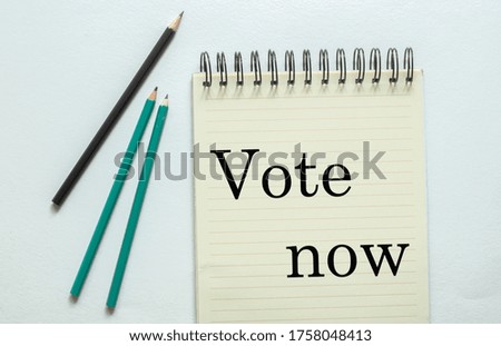 two green one black pencil with text "Vote now " in the notebook on the white background