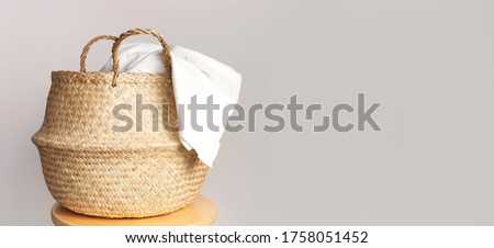Straw wicker basket and white natural cotton fabric, towel on gray background. Fashionable bamboo basket stylish interior item eco design handmade. Decor of home. Natural eco materials, storage basket Royalty-Free Stock Photo #1758051452