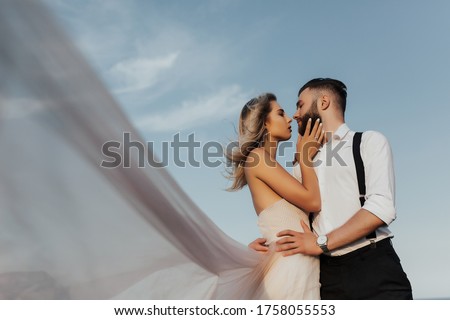 Portrait of couple looking each other on a background of blue sky. Bride and groom kisses tenderly in the shadow of a flying veil .Beautiful picture. Copy space.