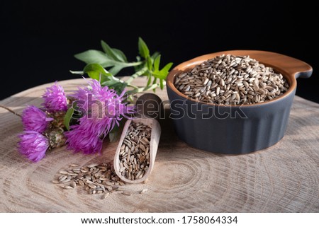 Milk thistle (Silybum marianum) seeds in wooden spoon and ceramic bowl, flowers on a wooden background. Medical plants. Alternative medicine.  Royalty-Free Stock Photo #1758064334