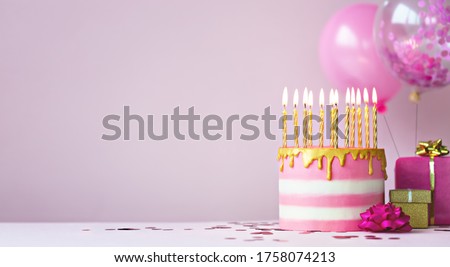 Pink birthday cake with golden candles and balloons