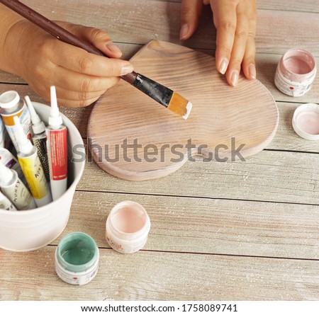female hand draws with a brush and acrylic paints on a sheet of wooden pine heat.Flat lay with woman's beautiful hands and trendy colors paints on rustic woody table. copy space.Handcraft wood concept Royalty-Free Stock Photo #1758089741