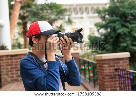 A young man hand-holding a camera while taking photos with a camera in a hotel conservatory