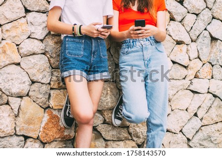 two teenagers of z or millennial generation using street telephones leaning on the wall, concept of influence and use of social networks