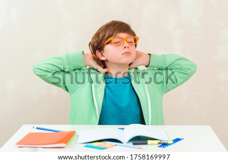 Tired schoolboy sitting at table. Boy doing homework. Learning difficulties, education concept. Stressed out and tired kid. Frustrated kid sitting at the desk with many books. Sad tired schoolchild.