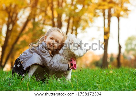 Child girl having fun with her dog during walk in autumn park. Little daughter playing with her west highland white terrier outdoors. Lifestyle portrait. Stylish little girl with pet at nature.