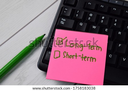 Long-term and Short-term write on a sticky note. Supported by an additional services isolated wooden table.