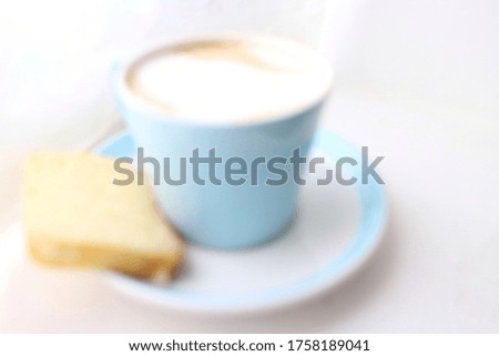 Soft Blurry defocused picture of a blue cup of coffee with milk on saucer with a piece of cake can be used as background with space for runaround or wraparound text 