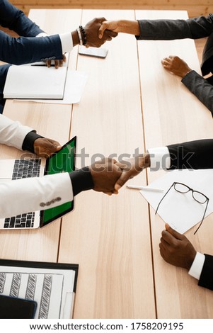 Top view of a table in an office as dark-skinned colleagues shake hands as a sign of cooperation against racism in the country and in the company.