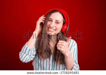 Gorgeous young woman is listening to the music through a headphones over red background.