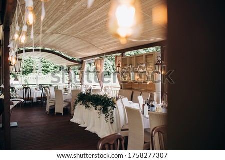 the inside of wedding tent. summer garden patio terrace decorated with lamp garlands with festive tables covered with white tablecloths and white chairs. place for a holiday in the outdoor.