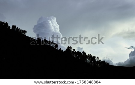 A silhouette shot of a hill with trees in front of the beautiful fluffy clouds