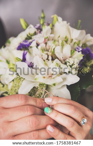 Hands of newlyweds with wedding rings and a bouquet of flowers. A bouquet of white cream roses and lilac flowers of the field. Concept of love wedding and Valentine's Day.