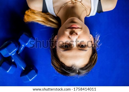 Young girl is doing fitness and different exercises in the gym.
Sport is health. Many sports equipment on  e background.
Themes of a healthy lifestyle. 
