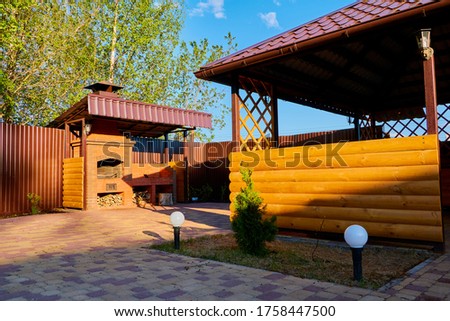 Wooden gazebo on the yard with greenery in a summer day