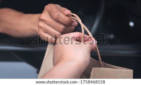 Closeup food delivery man driver’s hand pass pick up environmentally friendly craft brown paper bag to customer out of car window meeting social distancing requirements and supporting small businesses Royalty-Free Stock Photo #1758468158
