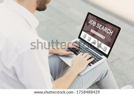 Looking For A Job. Back view over the shoulder of man using laptop with vacancies website on monitor, typing on keyboard