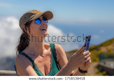 Smiling woman in the cap and sunglasses taking selfie photo on the cloud background