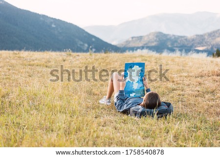 Female traveler consulting map lying on the grass among mountains