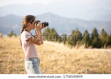 Caucasian girl taking photos in the field at sunset with mountains in the background