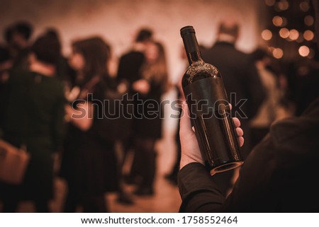 man dressed in black holds a bottle of wine in his hand
