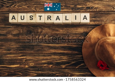 top view of artificial flower, felt hat and australian flag near cubes with australia lettering on wooden surface, anzac day concept