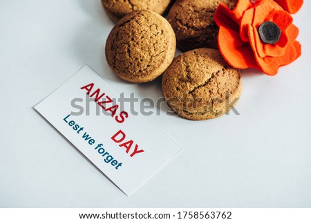 card with anzas day lettering near artificial flower and cookies on white