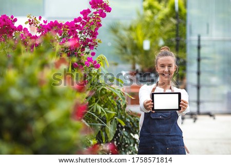 Female Garden Worker Holding an blank tablet PC. Attractive young woman in a flower center.  Young woman working in flower garden. Woman entrepreneur