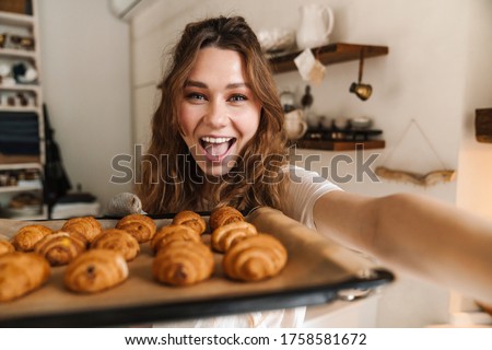 Cheerful young girl taking a selfie and showing baked cookies from the oven