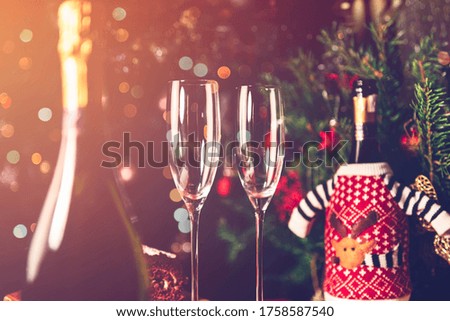 Two empty flute glasses and bottles of champagne in preparation for Xmas or New Year party. One bottle is in the christmas jumper and xmas tree on the background
