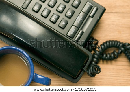 A black telephone and a cup of coffee on a wooden table